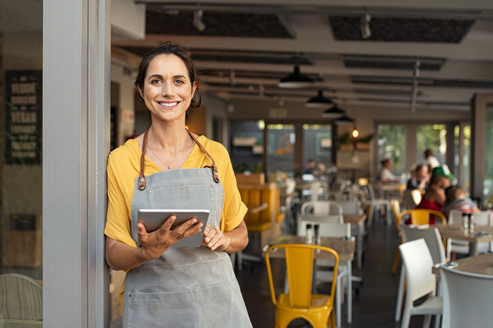 Woman business owner standing in front of cafe with an ipad.