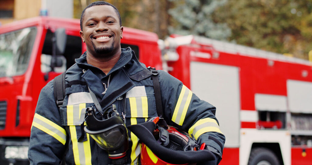 Smiling Firefighter in uniform standing besides a firetruck